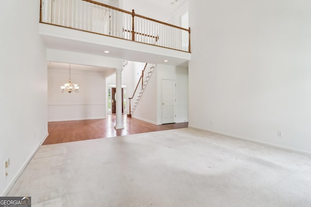 unfurnished living room featuring a notable chandelier, carpet floors, stairs, baseboards, and a towering ceiling