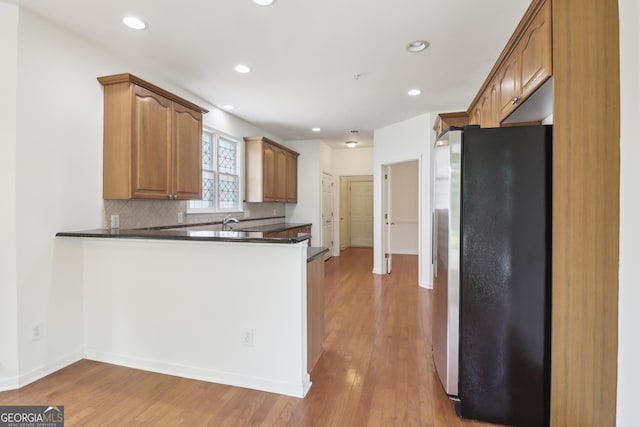 kitchen featuring freestanding refrigerator, light wood-style flooring, baseboards, dark countertops, and tasteful backsplash