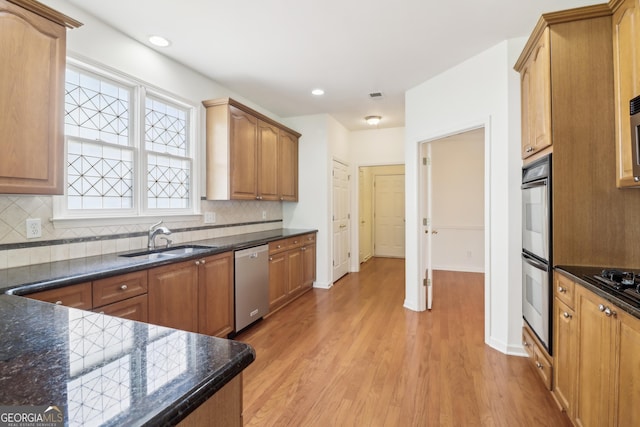 kitchen featuring light wood-style floors, a sink, appliances with stainless steel finishes, and tasteful backsplash