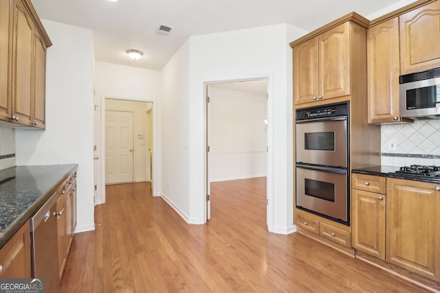 kitchen with appliances with stainless steel finishes, light wood finished floors, dark stone counters, tasteful backsplash, and visible vents