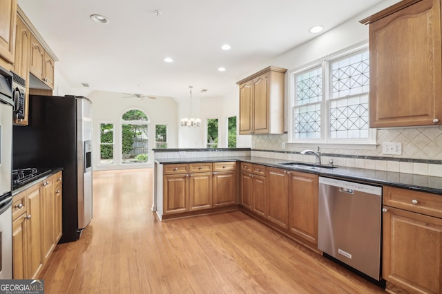 kitchen with a peninsula, a sink, light wood-style flooring, backsplash, and stainless steel appliances