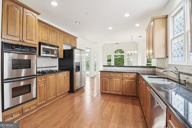 kitchen with recessed lighting, a sink, dark stone countertops, light wood-style floors, and stainless steel appliances