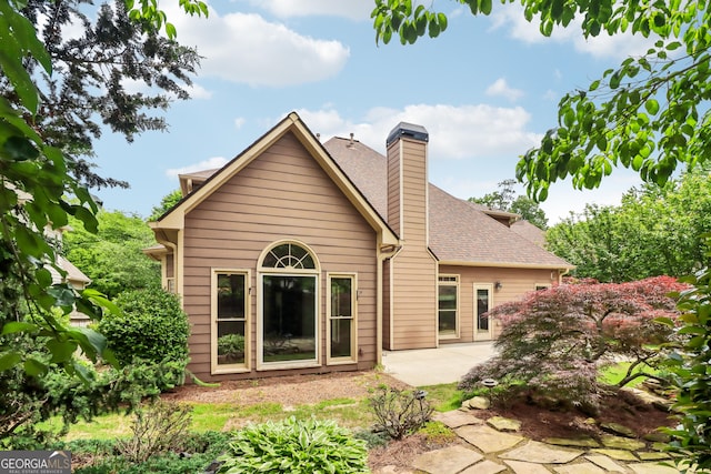 back of property with a patio area, roof with shingles, and a chimney