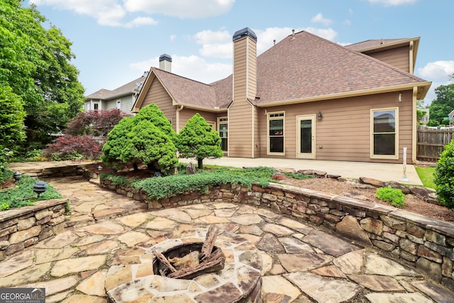 back of property with a chimney, roof with shingles, fence, an outdoor fire pit, and a patio