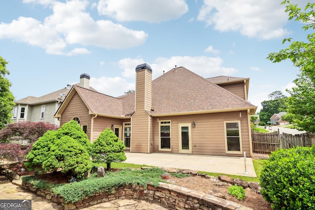 rear view of house featuring a patio, fence, a shingled roof, and a chimney