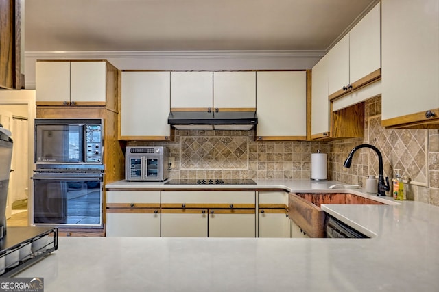 kitchen featuring light countertops, decorative backsplash, black appliances, and under cabinet range hood
