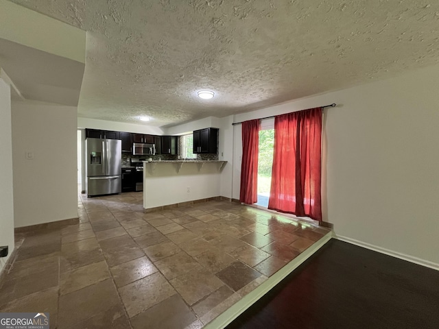 unfurnished living room with baseboards, stone tile floors, and a textured ceiling
