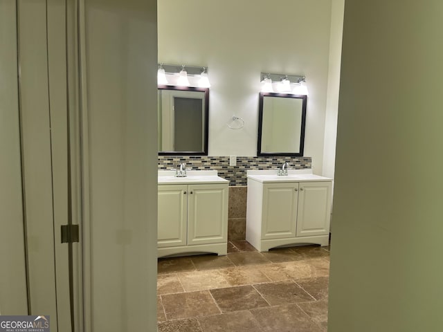 full bath featuring stone tile flooring, a sink, two vanities, and tile walls