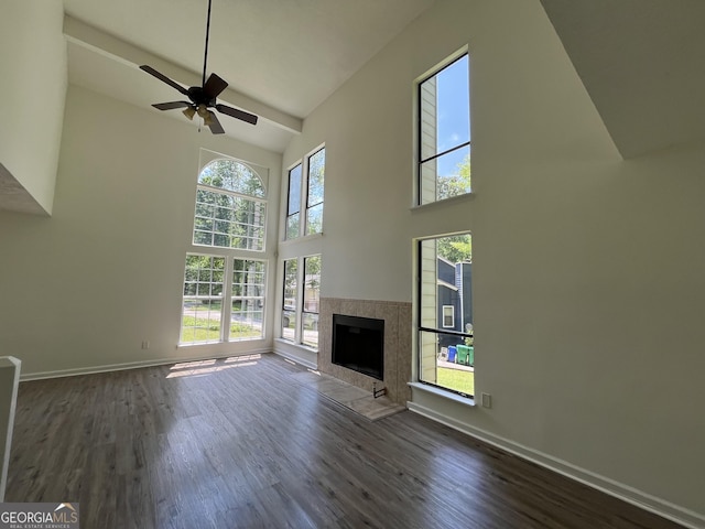 unfurnished living room with baseboards, wood finished floors, high vaulted ceiling, and a tile fireplace