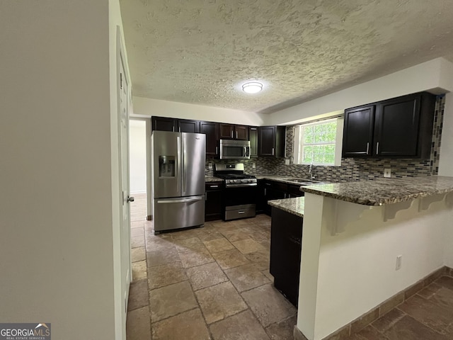 kitchen featuring a sink, a breakfast bar area, stainless steel appliances, a peninsula, and decorative backsplash