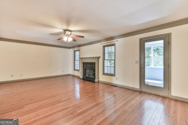 unfurnished living room featuring ceiling fan, a tiled fireplace, light wood-style flooring, baseboards, and ornamental molding