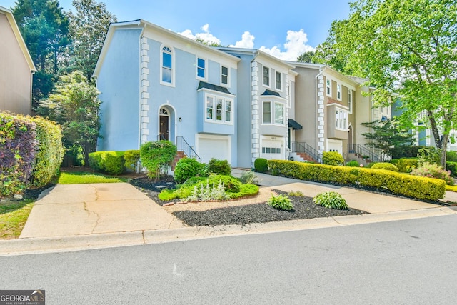 townhome / multi-family property with stairway, an attached garage, and stucco siding