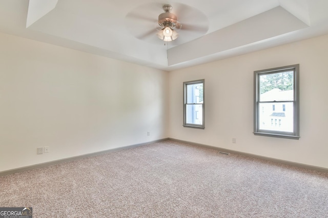 carpeted spare room featuring baseboards, plenty of natural light, a tray ceiling, and ceiling fan