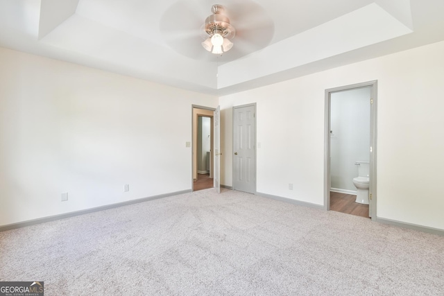 unfurnished bedroom with carpet flooring, ceiling fan, a raised ceiling, ensuite bath, and baseboards