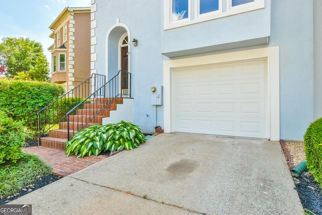 entrance to property with stucco siding, driveway, and a garage