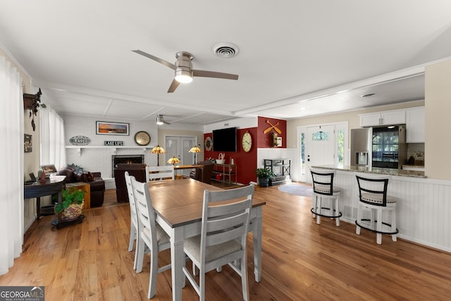 dining room featuring visible vents, light wood finished floors, a brick fireplace, and ceiling fan