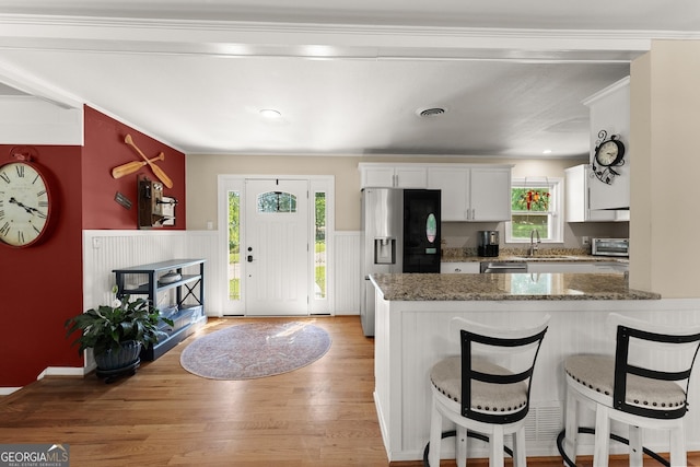 kitchen with a kitchen breakfast bar, white cabinetry, a sink, light wood finished floors, and stainless steel appliances