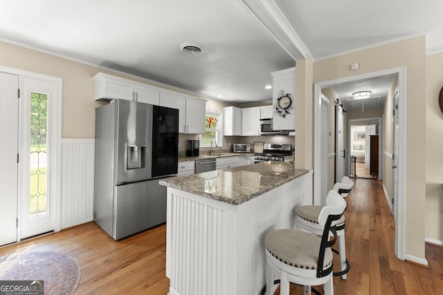 kitchen featuring white cabinets, crown molding, appliances with stainless steel finishes, a kitchen breakfast bar, and stone countertops