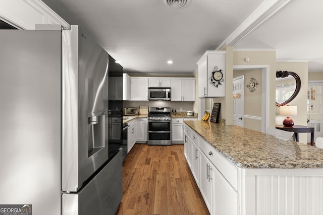 kitchen with crown molding, a peninsula, white cabinets, light wood-style flooring, and stainless steel appliances