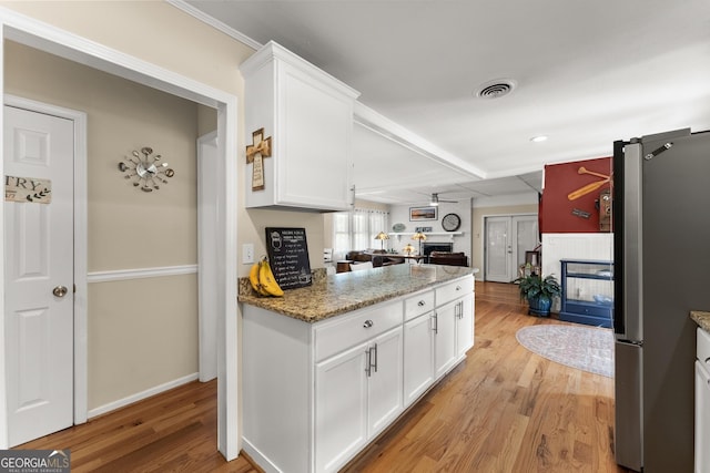 kitchen with ceiling fan, a fireplace, light wood-type flooring, freestanding refrigerator, and white cabinetry