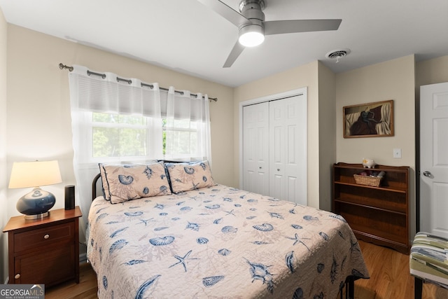 bedroom with a ceiling fan, visible vents, wood finished floors, and a closet