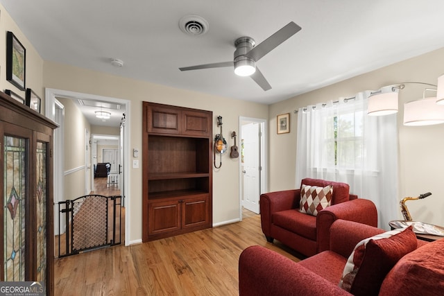 living area with visible vents, baseboards, attic access, a ceiling fan, and light wood finished floors