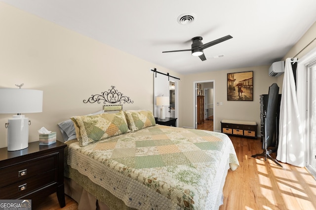 bedroom with ceiling fan, a wall unit AC, visible vents, a barn door, and light wood finished floors