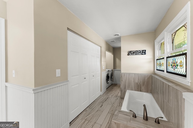 bathroom featuring wood finished floors, a bath, wainscoting, and washing machine and dryer