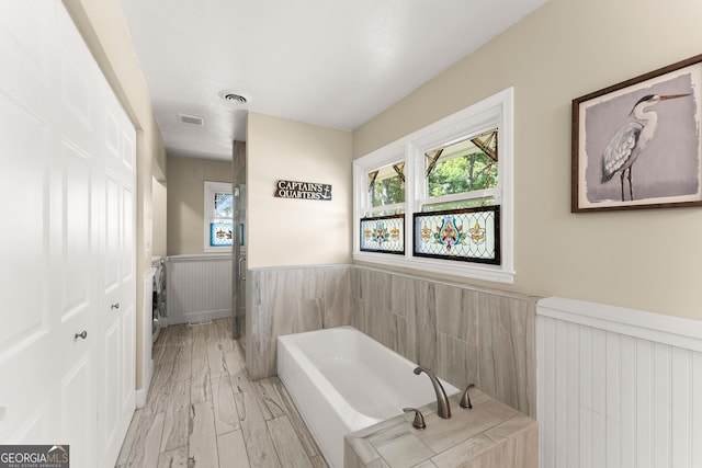 full bath with a bath, visible vents, wainscoting, radiator, and a wealth of natural light
