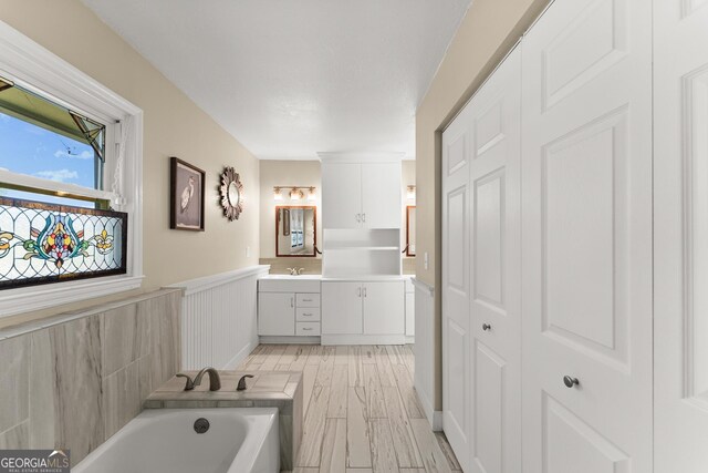 full bathroom featuring vanity, a wainscoted wall, a bathtub, and wood finished floors