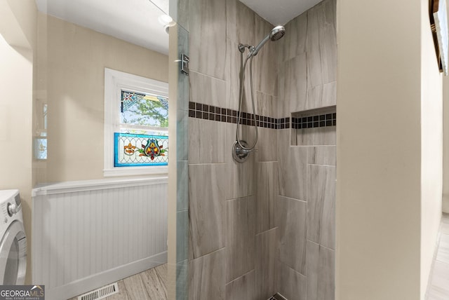 bathroom with visible vents, washer / dryer, wood finished floors, and tiled shower