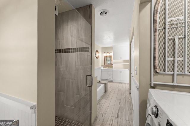 full bathroom featuring washer and dryer, wood finish floors, vanity, a shower stall, and visible vents