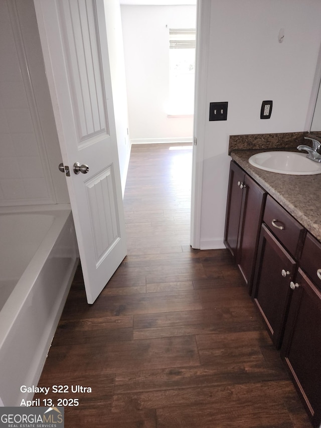 bathroom with a bath, baseboards, vanity, and wood finished floors