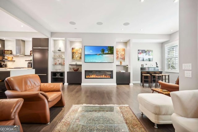 living room with built in shelves, wood finished floors, baseboards, a glass covered fireplace, and recessed lighting