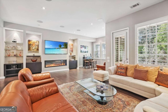 living room with visible vents, a glass covered fireplace, wood finished floors, baseboards, and built in shelves