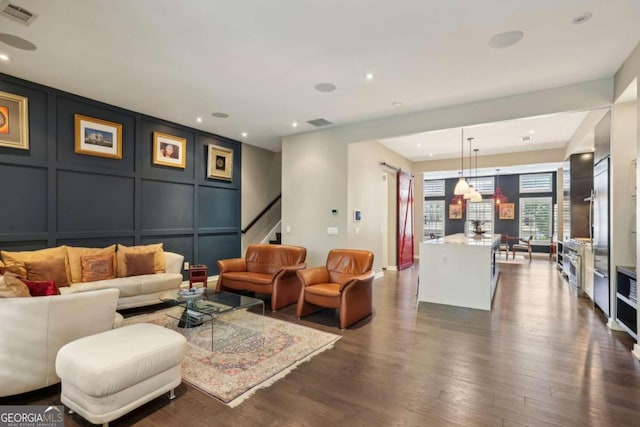 living area with dark wood-style flooring, visible vents, stairs, a decorative wall, and recessed lighting