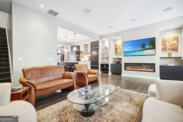 living area featuring visible vents, built in shelves, wood finished floors, a glass covered fireplace, and stairs