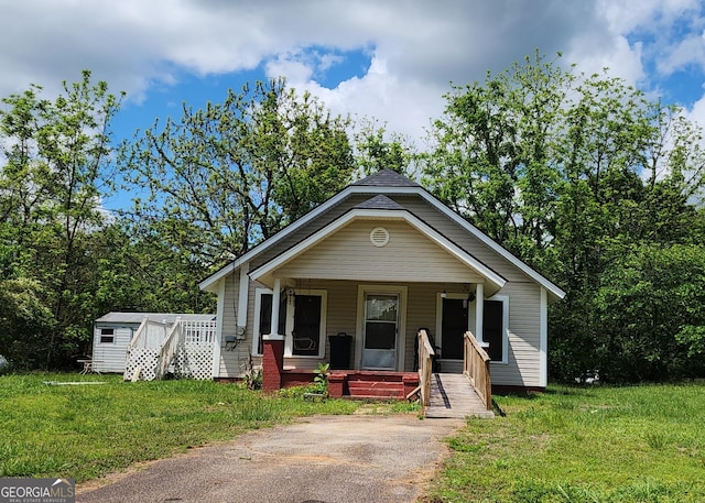 bungalow-style house with a porch, an outdoor structure, a front lawn, and a storage unit