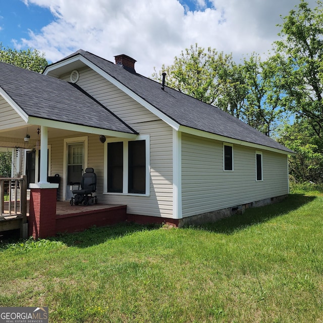 back of house featuring a yard, roof with shingles, a chimney, and a porch