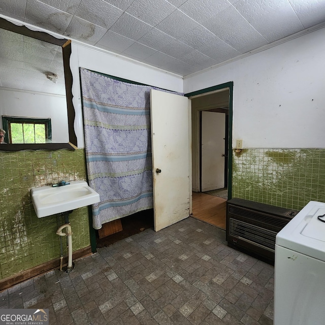 bathroom featuring a sink, tile walls, wainscoting, washer / dryer, and brick patterned floor