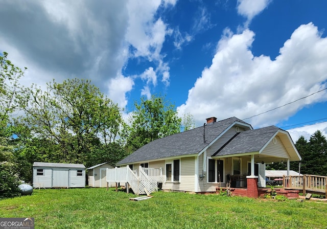 view of front of home featuring a storage unit, a chimney, an outdoor structure, a front yard, and roof with shingles