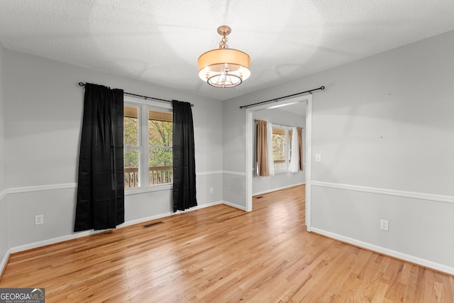empty room with baseboards, an inviting chandelier, wood finished floors, and visible vents