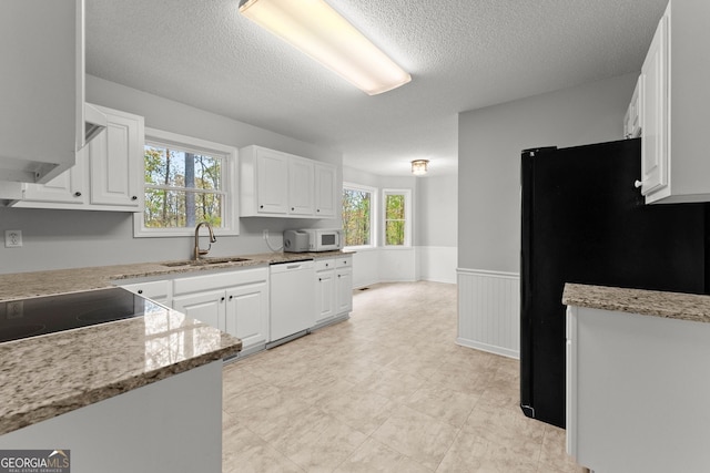 kitchen featuring a textured ceiling, a sink, a wainscoted wall, white cabinets, and white appliances