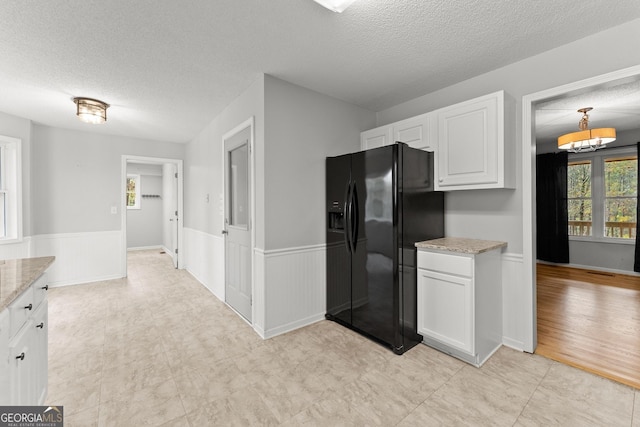 kitchen featuring black fridge, wainscoting, a textured ceiling, and a wealth of natural light