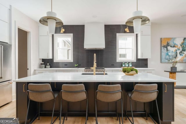 kitchen with high quality fridge, light countertops, white cabinets, custom range hood, and backsplash