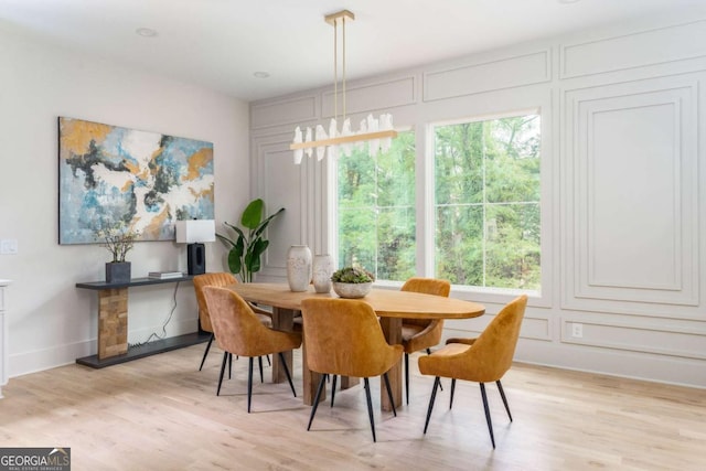 dining area featuring light wood-type flooring, baseboards, and a decorative wall