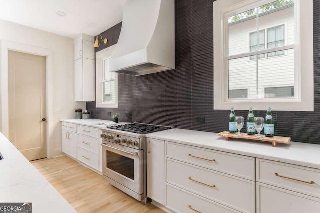 kitchen with light countertops, decorative backsplash, stainless steel stove, and premium range hood