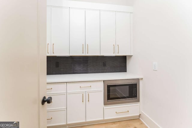 bar with backsplash, baseboards, built in microwave, and light wood-type flooring