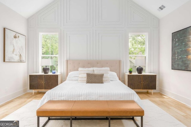 bedroom with light wood-style floors, multiple windows, vaulted ceiling, and visible vents