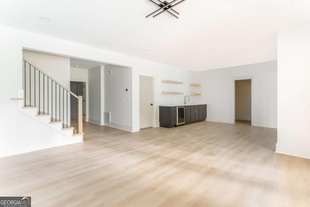 unfurnished living room featuring light wood-style floors, beverage cooler, baseboards, visible vents, and stairway